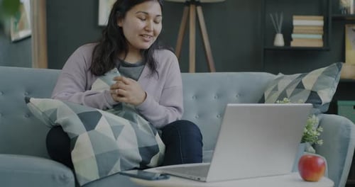 Fröhliche asiatische Frau benutzt Laptop, tätigt Videoanrufe, spricht und winkt zu Hause mit der Hand