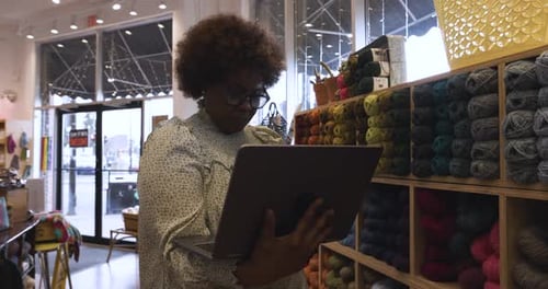 Female Business Owner with Laptop Checking Inventory in Yarn Store 5054 Years