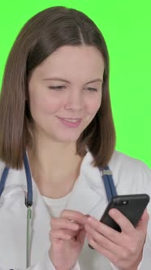 Female Doctor Browsing Smartphone on Green Background, vertical video