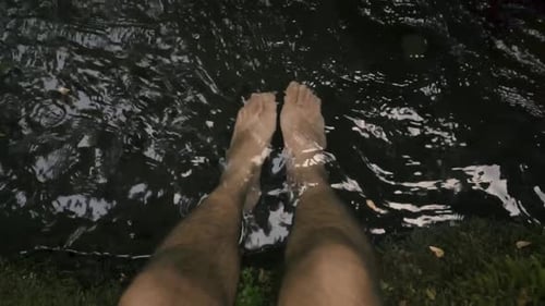 Point of view of a man's feet sitting at the river with his feet in the water.