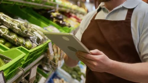 Man Uses Tablet in Front of Produce Shelves