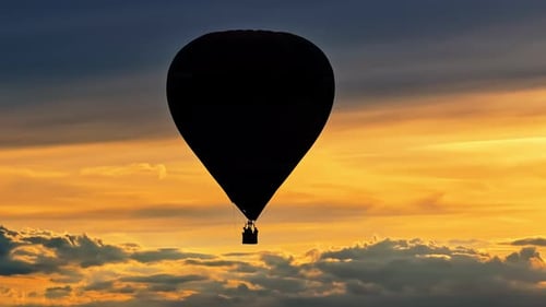 Aerial drone view of a hot air balloon flying above the clouds at sunset