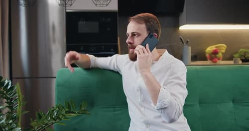 Homme parlant à l'aide d'un téléphone portable, assis sur un canapé dans la cuisine. Contact sur smartphone, discussion, conversation