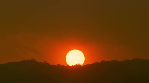 Time lapse of a large orange sun sets on a mountain.