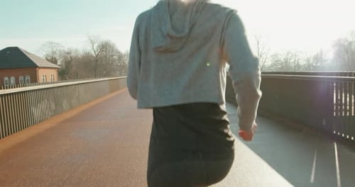 Unrecognizable sporty woman running on empty road in sunlight for fitness training