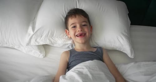 Adorable Child Hides in Bed Under White Sheets