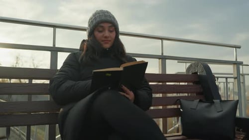 Woman Reads Book on Bench on Overcast Day