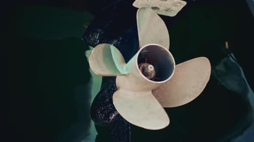 Close up view of a marine metal propeller partially submerged, showing rust, patina, and subtle refl