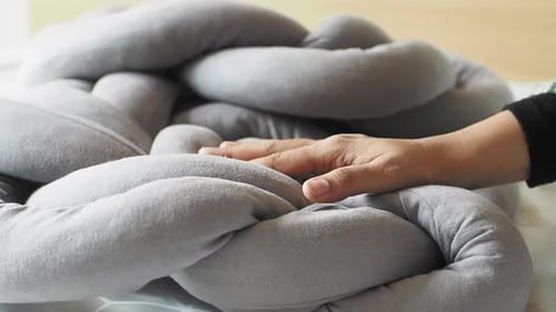 Hand Touches a Gray Braided Decorative Pillow