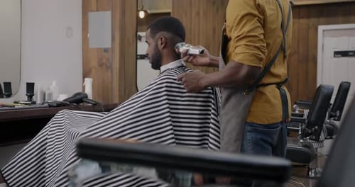 Side View of Skilled Barber Shaving Client with Machine Creating Modern Hairstyle in Barbershop