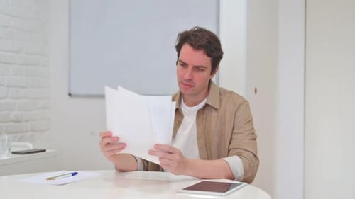 Young Man Reviews Documents in Office, Gets Frustrated
