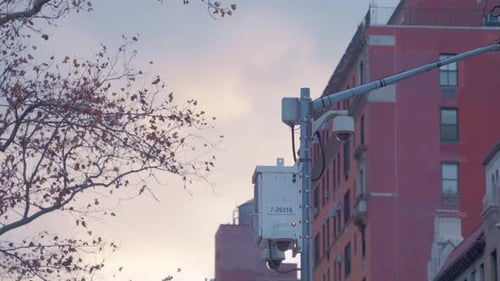 A mounted security camera watches over a quiet New York City street as the evening sky glows with so