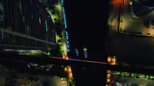 Bigger and smaller yachts move by the dark river at night.