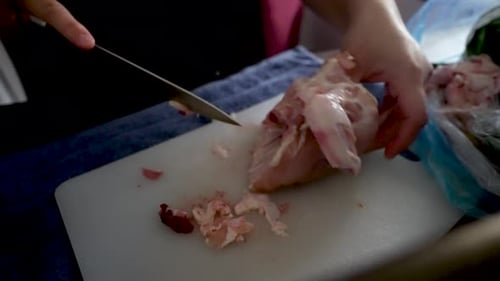 Chef découpant du poulet cru sur une planche à découper, préparant un plat de volaille
