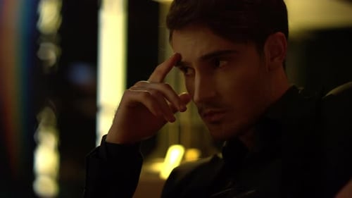 Thoughtful man in dim lighting, holding finger to forehead