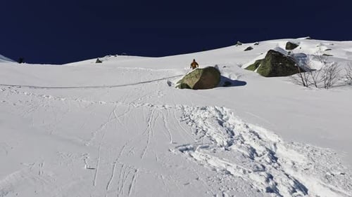 Skier Performs Backflip off Rocky Ledge in Snowy Mountains