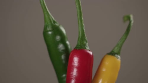 Closeup of green, red, and yellow chili peppers pulls out to defocus on grey.