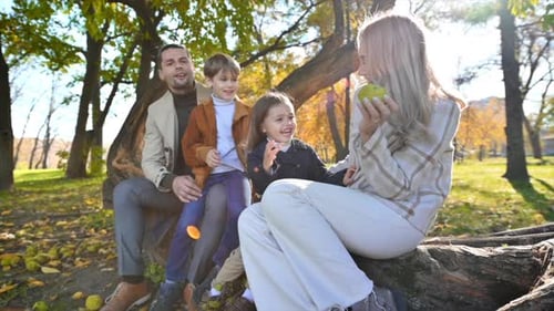 Happy family in an autumn park. Mother, father, son and daughter sitting on a tree trunk, mom playin
