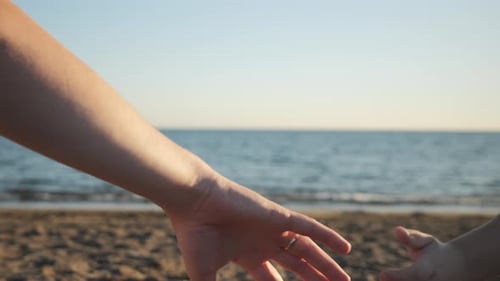 Die Hand eines Mannes nimmt die Hand eines Kindes am Meeresstrand