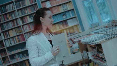 Happy Young Woman is Spending Her Free Time at Bookstore Looking for a New Book to Buy