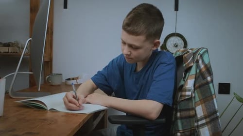 Schoolboy Sits at Computer Takes Notes in Copybook During Distant Learning