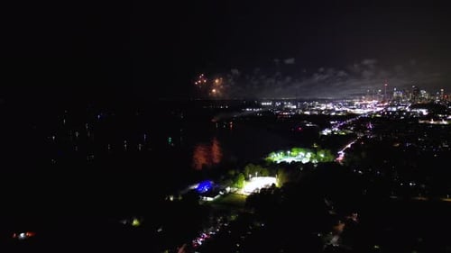 Fireworks pyrotechnic show reflections in lake water near urban neighbourhood with city skyline from