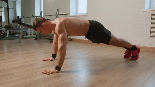 Bodybuilder in Black Shorts and Red Sneakers is Training in Gym and Doing Exercises Plank Sport and