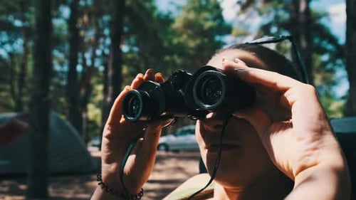 Woman Uses Binoculars While Camping in Forest