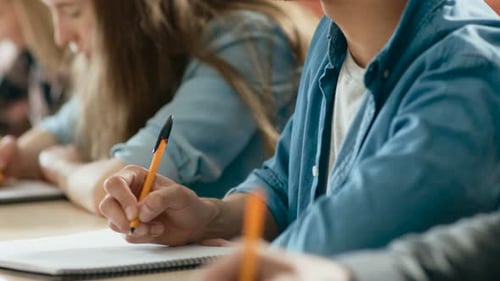 Close-up of the Row of Students Writing in the Notebooks, Taking Exam. Focus of Hands with Pens.