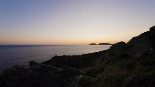 Colourful sunset over beautiful rocky coastline and calm ocean water