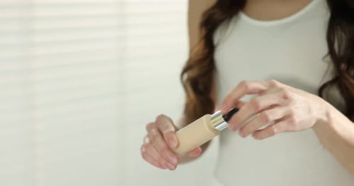 Woman Opening Bottle of Beige Liquid Foundation