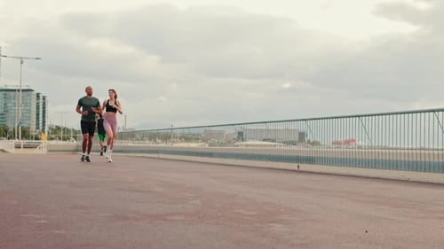 Panorama side view of young active couple jogging together along the beach