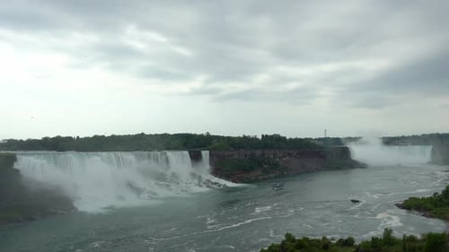 Landscape view of Niagara Falls, water flowing down the waterfall creating steam, on a cloudy day