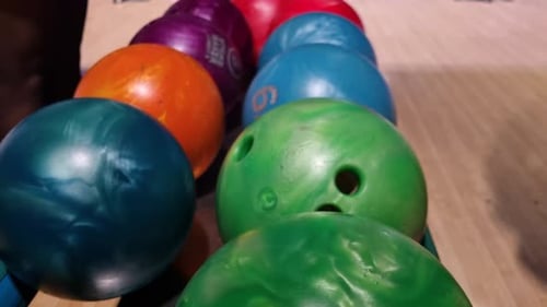 Bright bowling balls rest in a neat row on the return rack inside a bowling alley