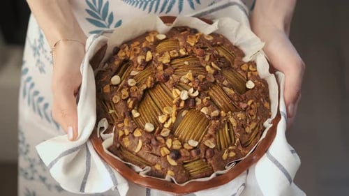 close-up woman holding a fresh open pie with pears and nuts