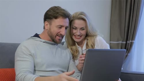 Smiling Couple Looking at Laptop on Sofa