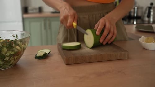 Woman's Hands are Shown Up Close As She Slices a Vibrant Green Zucchini on a Wooden Cutting Board in
