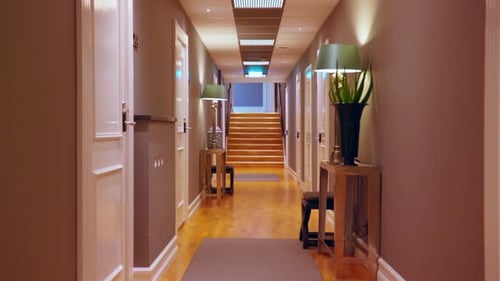 Smooth tracking shot down a stylish hotel corridor featuring white doors, warm wood-paneled walls, a
