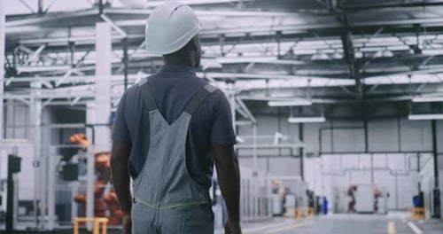 Male Factory Worker Observing Robotic Systems and Automated Assembly Lines of Modern Facility