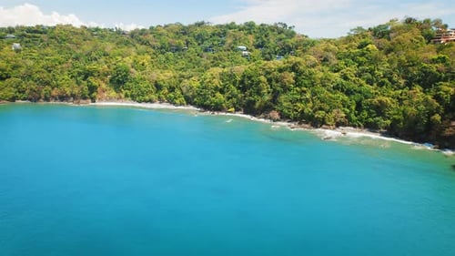 Turquoise ocean waves gently hit the forested sandy shoreline in Costa Rica