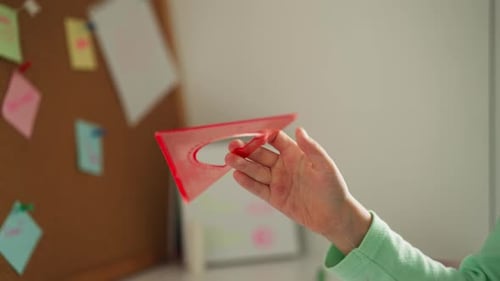 Little Girl Spins Pink Squareruler in Fingers Near Corkboard