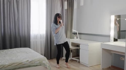 Woman Singing and Dancing with Hairbrush in Bedroom