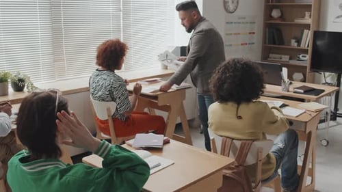 Teacher Passing Out Assignments to Students in Classroom