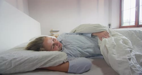 Young Woman Waking Up and Stretching in Bed