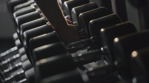 A Sporty Man is Taking Heavy Dumbbells From the Rack