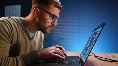 Side view. Male programmer is working indoors by a laptop.