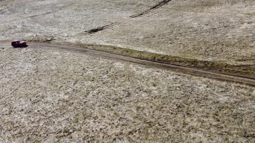 Orange SUV passing through fields aerial view.