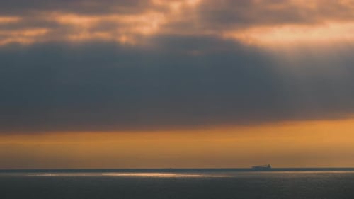 Beautiful Light Rays Shining Through Gaps in Clouds Over Ocean with Silhouetted Tanker Ship