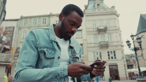 Close Up Serious Young African American Man Uses the Phone Sitting Outdoor at the Street Business