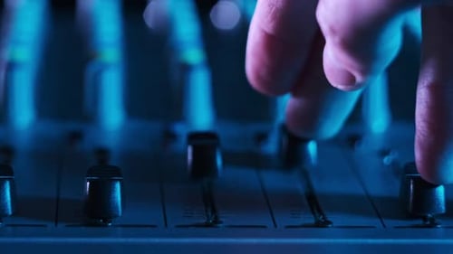 Hand Settings Volume Level Controls on Mixing Console Faders Neon Light CloseUp